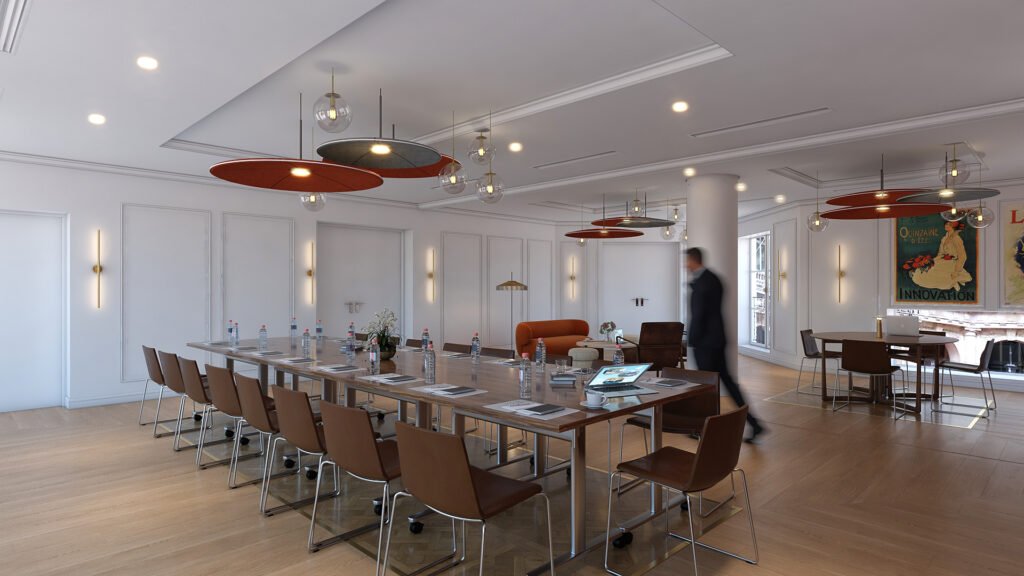 Salle de réunion moderne et élégante avec une grande table centrale entourée de chaises en cuir marron, équipée de bouteilles d’eau, ordinateurs et carnets. L’espace est éclairé par des suspensions design et dispose d’un coin lounge avec fauteuils et affiches rétro aux murs. Un homme en costume flou traverse la pièce, suggérant une ambiance professionnelle et dynamique.